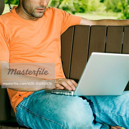 Close-up of a young man using a laptop on a porch swing