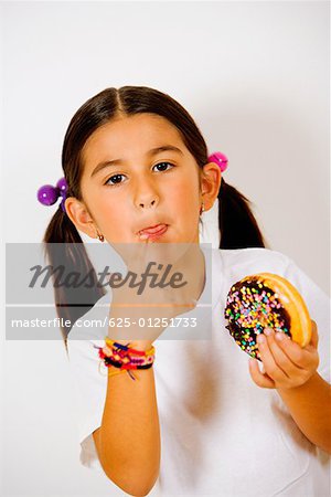 Portrait d'une jeune fille tenant un beignet et lécher son doigt