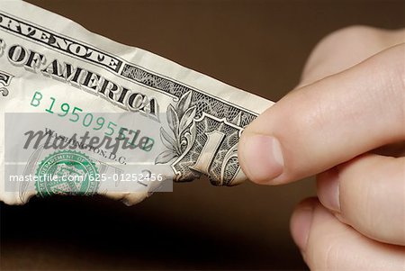 Gros plan des doigts d'une personne détenant un billet d'un dollar américain brûlé