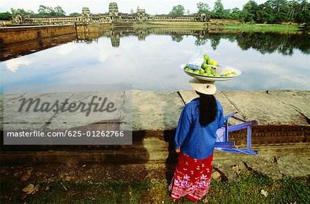 Rear view of a female vendor carrying lime fruit on her head, Angkor Wat, Angkor, Siem Reap, Cambodia