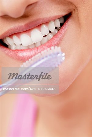 Gros plan d'une jeune femme souriante avec une brosse à dents devant sa bouche