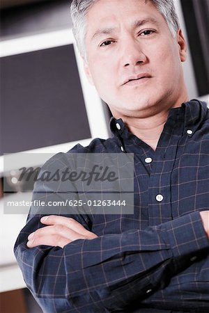 Portrait of a senior man standing with his arms folded in front of a computer