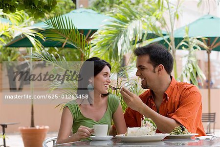 Mid adult man feeding a teenage girl with a fork at a restaurant