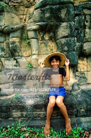Boy sitting on a ledge and smiling, Angkor Thom, Angkor, Siem Reap, Cambodia