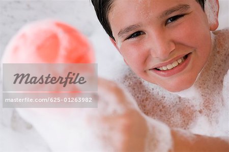 Portrait d'un garçon tenant une boule dans une baignoire et souriant