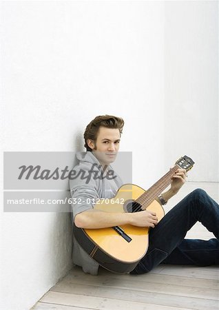 Jeune homme assis sur le plancher, jouer de la guitare