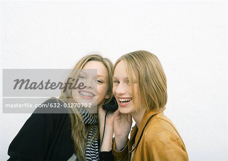 Two young female friends sharing headphones, smiling at camera