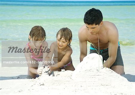 Père et ses deux enfants jouant dans le sable sur la plage