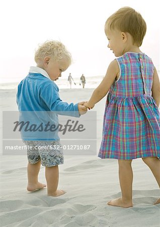 Two toddlers standing on beach, rear view