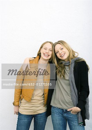 Zwei jungen Freundinnen, eine mit Arm um die Schultern der anderen beiden lächelnd in die Kamera