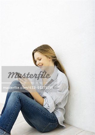 Teenage girl using cell phone, sitting on floor