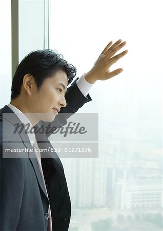 Businessman looking out of window of high rise, side view