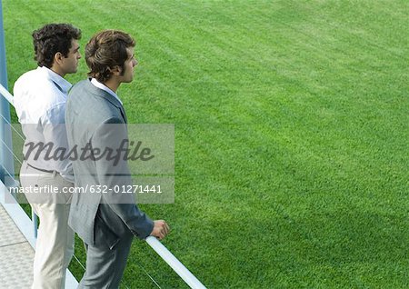Two businessmen standing on walkway, looking into distance