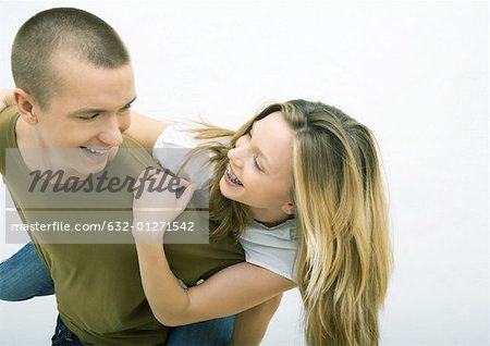 Young couple, man holding young woman on back, looking over shoulder, smiling at each other