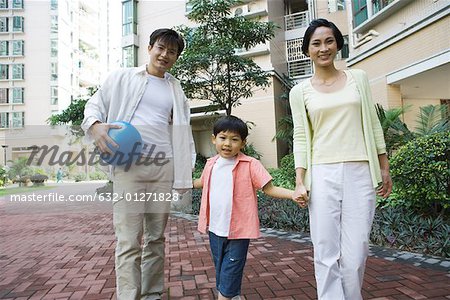 Family standing by apartment complex, smiling at camera, father holding ball