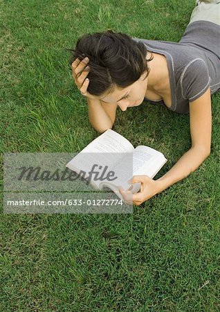 Woman lying in grass, reading book