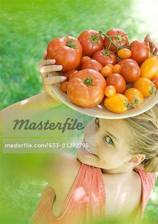 Jeune femme brandissant bol de tomates, souriant à la caméra