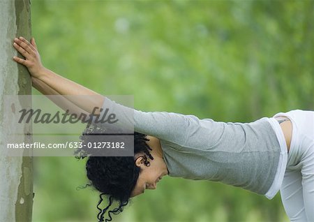 Young woman stretching against tree