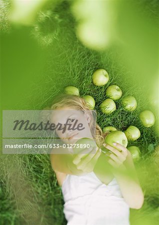 Femme couchée dans l'herbe, tenant des pommes vers la caméra