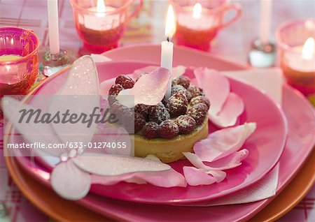 Himbeer Kuchen auf Teller dekoriert mit Rosenblätter und Kerzen