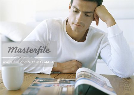 Man sitting at table, looking at book, with coffee cup