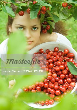 Woman holding bowl of cherries, standing under cherry tree