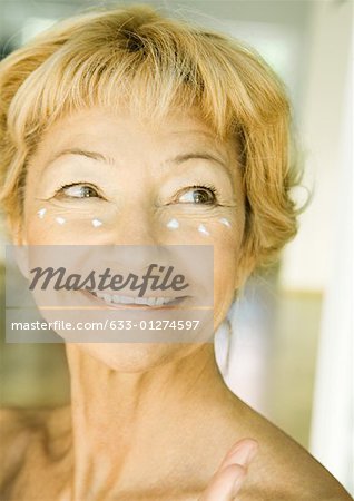 Femme Senior avec cuillerées de crème hydratante sous les yeux