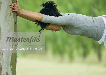 Young woman stretching against tree trunk