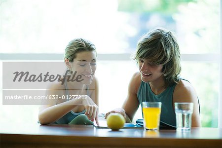 Young adults in exercise clothing, having snack in health club cafeteria, looking at magazine