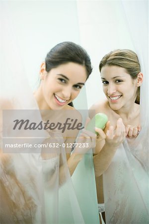 Two young women taking showers, one handing the other a bar of soap