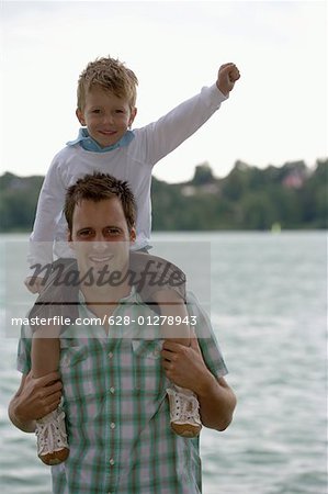 Milieu adulte homme est debout devant un lac avec un garçon sur ses épaules, mise au point sélective