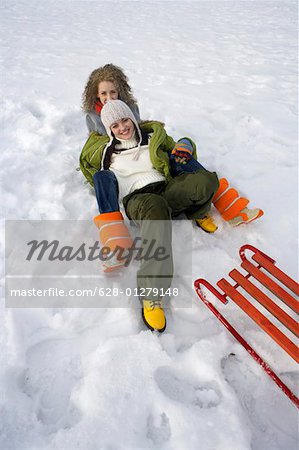 Two young women lying in the snow behind a sled