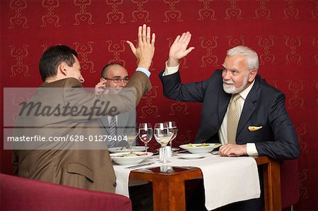 Three businessmen cheering during a business lunch