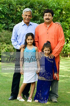 Portrait of a senior man with his son and two granddaughters standing in a garden and smiling