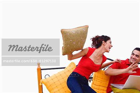 Young woman swinging a cushion at a young man