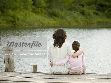 Rear view of a woman and her daughter sitting on a pier