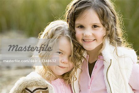 Portrait of two girls smiling and hugging outdoors