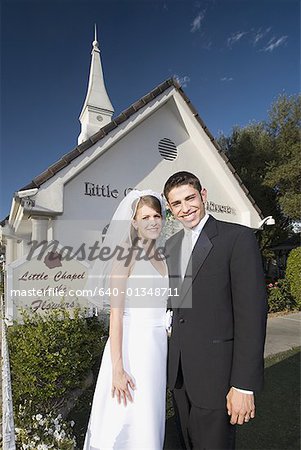 Portrait d'un couple de jeunes mariés, debout devant une chapelle et souriant