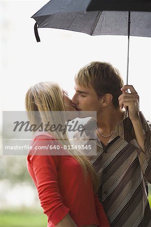 Teenage couple kissing under an umbrella