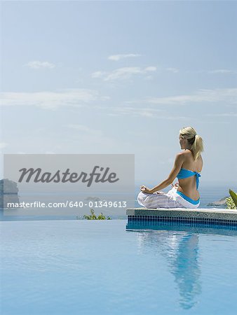 Rear view of a mid adult woman sitting in a lotus position at the poolside