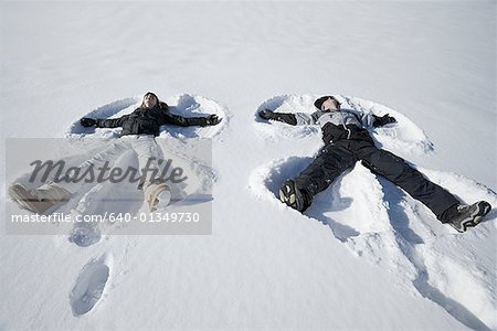 Vue grand angle sur un jeune couple couché dans la neige, faire des anges de neige