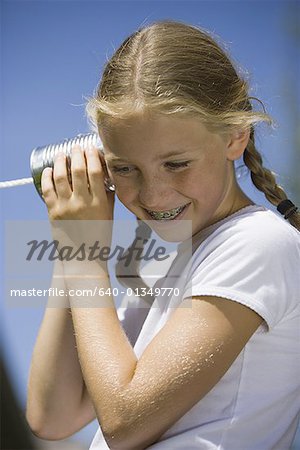 Vue d'angle faible d'une fille à l'écoute sur un téléphone de boîtes de conserve