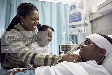 Gros plan d'un petit garçon couché sur un lit d'hôpital et sourit à sa mère et sa sœur