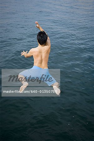 Rear view of a young man jumping in a lake