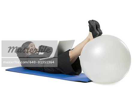 Geschäftsfrau, die mit einem Laptop während des Trainings auf einem Fitness-ball