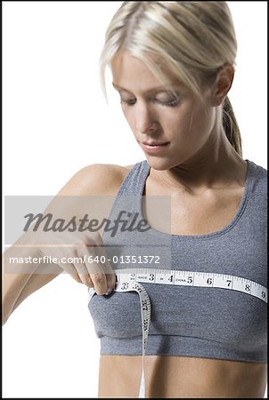 Une jeune femme mesurant sa poitrine avec un ruban à mesurer