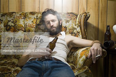 Homme sur le canapé avec une bouteille de bière et cigarettes