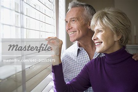 Mature couple looking through blinds of a window