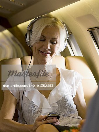 A businesswoman listening to music from an MP3 player in an airplane