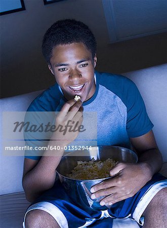 Teenage boy watching television and eating popcorn